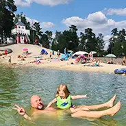 fröhlich posierender Papa mit Tochter im Badesee, Südsee-Camp Strand, Leuchtturm und weitere Familien im Hintergrund