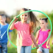 Mädchen mit Hulahoop-Reifen in der Hand, Kinder im Hintergrund