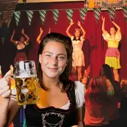 Frau im Dirndl mit Bierkrug, tanzende Personen im Hintergrund