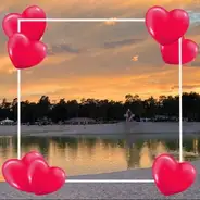 Sonnenuntergang über dem See mit Leuchtturm umgeben von einem Herzrahmen